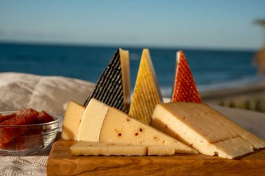 İspanyol sert peynirleri, curado, manchego, keçi peyniri arka planda mavi denizli membrillo reçeli servis edilir.