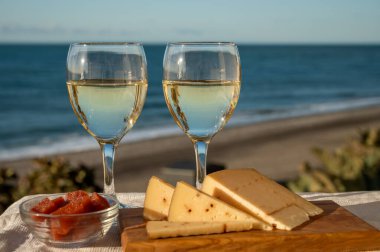 İspanyol sert Endülüs peyniri tatlı şeri ile dolu açık havada servis edilen membrillo reçeli iki bardak beyaz şarap ve arka planda mavi deniz, yakın çekim.