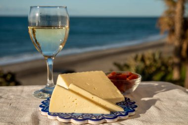 İspanyol sert keçi peyniri, açık havada membrillo reçeli ve arka planda mavi deniz bulunan bir bardak beyaz şarapla servis edilir.