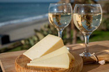 İspanyol sert manchegosu, inek, koyun ve keçi peyniri güneşli bir günde açık havada beyaz şarap ve mavi deniz manzarasıyla servis edilir.