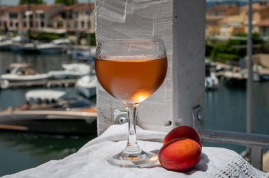 Drinking of cold rose wine from Provence with red apricots and view on yacht harbour of Port Grimaud, summer vacation on French Riviera, France