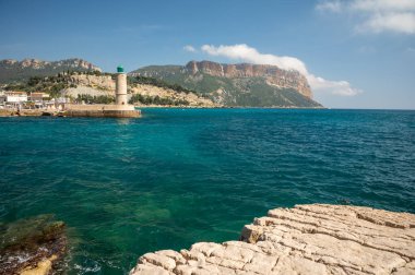 Kumsalda panoramik manzara, mavi deniz, uçurumlar, evler, sokaklar ve bulutlu bir günde Cassis, Provence, Fransa 'da deniz feneriyle eski balıkçıların limanı
