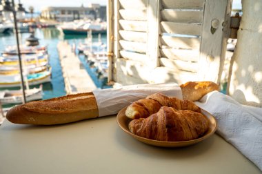 Provence 'de yaz sabahı, taze kruvasan ve baget ekmeği ile geleneksel kahvaltı Cassis, Provence, Fransa Limanı' ndaki balıkçı teknelerinin manzarası.
