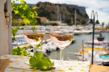 Açık terasta sunulan Rose Provencal şarabı Cassis, Provence, Fransa 'da renkli tekneleri olan eski balıkçıların limanına bakıyor.