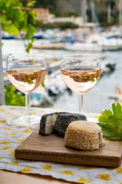 Bardakta Rose Provencal şarabı, açık terasta keçi peyniri ve Cassis, Provence, Fransa 'da renkli tekneleri olan eski balıkçıların limanına bakan manzaralı.