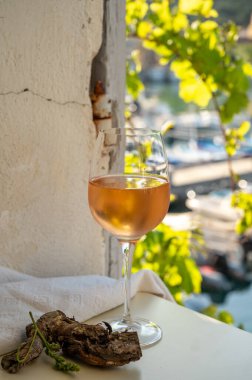 Soğuk gül şarabı, cam içinde sunulan güneş ışığı eşliğinde açık terasta, Cassis, Provence, Fransa 'da eski balıkçıların limanında renkli teknelerle sunuluyor.