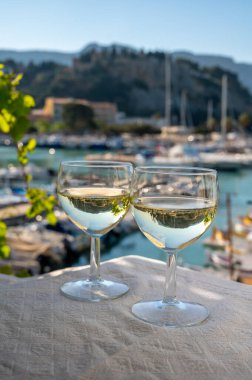 Cassis şaraplarından elde edilen iki bardak beyaz şarap, Fransa, Provence, Cassis 'te renkli tekneli eski balıkçıların limanı manzaralı terasta servis edilir.