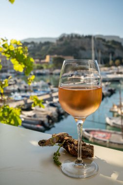 Soğuk gül şarabı, cam içinde sunulan güneş ışığı eşliğinde açık terasta, Cassis, Provence, Fransa 'da eski balıkçıların limanında renkli teknelerle sunuluyor.