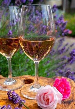 Provence 'den Fransız gülü şarabı, arka planda mor lavanta çiçekli iki kadeh şarap güneşli bir günde açık havada zeytin ağacı tahtasında servis ediliyor.