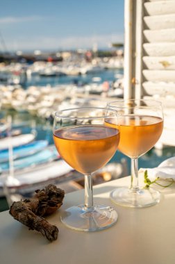 Soğuk gül Provencal şarabı bardaklarla sunuluyor. Açık terasta sunuluyor. Eski balıkçıların limanında, Cassis, Provence, Fransa 'da renkli tekneleri var.
