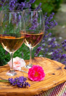 Provence 'den Fransız gülü şarabı, arka planda mor lavanta çiçekli iki kadeh şarap güneşli bir günde açık havada zeytin ağacı tahtasında servis ediliyor.