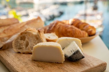 Provence 'de güneşli bir sabah, taze kruvasan, baquett ekmeği, crottin keçi peyniri ve Cassis, Provence, Fransa limanındaki balıkçı tekneleri manzaralı bir kahvaltı.