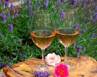 Provence 'den Fransız gülü şarabı, arka planda mor lavanta çiçekli iki kadeh şarap güneşli bir günde açık havada zeytin ağacı tahtasında servis ediliyor.