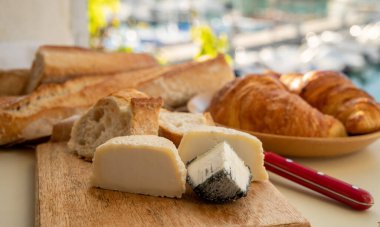 Provence 'de güneşli bir sabah, taze kruvasan, baquett ekmeği, crottin keçi peyniri ve Cassis, Provence, Fransa limanındaki balıkçı tekneleri manzaralı bir kahvaltı.