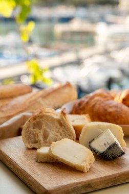 Provence 'de güneşli bir sabah, taze kruvasan, baquett ekmeği, crottin keçi peyniri ve Cassis, Provence, Fransa limanındaki balıkçı tekneleri manzaralı bir kahvaltı.