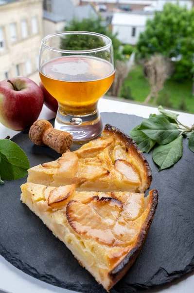 Apple products of Normandy region, homemade baked apple cake, glass of cider drink and houses of Etretat village on background, Normandy, France