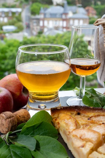 Apple products of Normandy region, homemade baked apple cake, glasses of calvados and cider drink and houses of Etretat village on background, Normandy, France