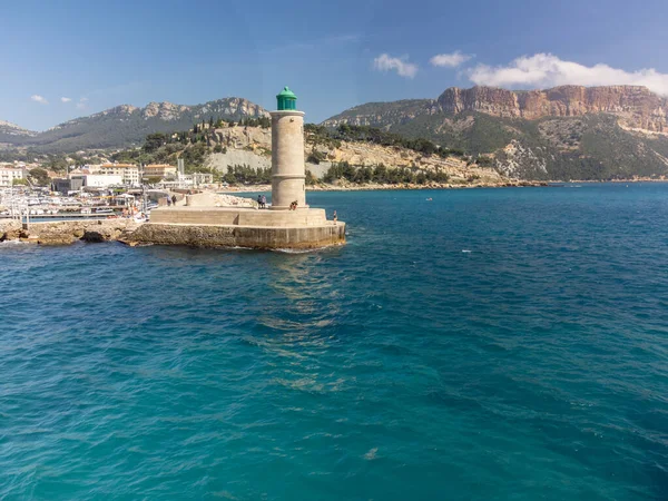 Panoramic aerial view on beach, blue sea, cliffs, houses, streets and old fisherman's harbour with lighthouse in Cassis, Provence, France in cloudy day