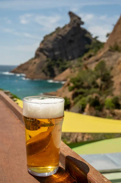 Glass of fresh cold lager beer served outdoor in snack bar with view on Calanque de Figuerolles in La Ciotat, Provence, France in sunny day