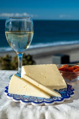 İspanyol sert keçi peyniri, açık havada membrillo reçeli ve arka planda mavi deniz bulunan bir bardak beyaz şarapla servis edilir.