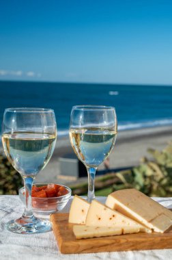 İspanyol sert Endülüs peyniri tatlı şeri ile dolu açık havada servis edilen membrillo reçeli iki bardak beyaz şarap ve arka planda mavi deniz, yakın çekim.