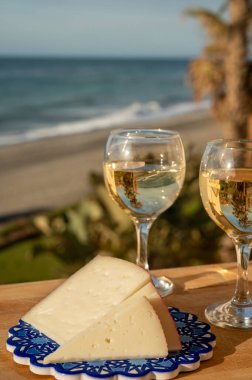 İspanyol sert manchegosu, inek, koyun ve keçi peyniri güneşli bir günde açık havada beyaz şarap ve mavi deniz manzarasıyla servis edilir.