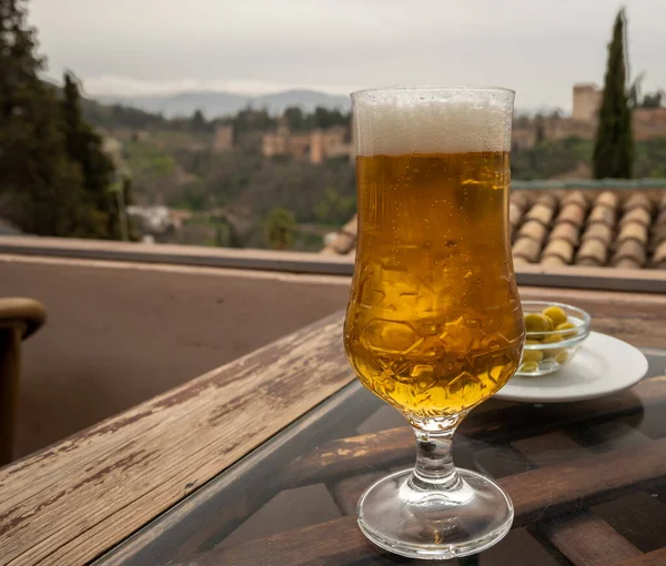 Spanish beer and glass bowl with green andalusian olives served on outdoor terrace with view on white Sierra Nevada mountains in Granada, Andalusia, Spain