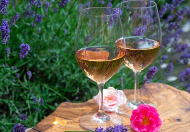 Provence 'den Fransız gülü şarabı, arka planda mor lavanta çiçekli iki kadeh şarap güneşli bir günde açık havada zeytin ağacı tahtasında servis ediliyor.
