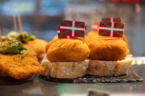Typical snack in bars of Basque Country, pinchos or pinxtos, small fried croquette with squid and flag of Basque Country, San Sebastian, Spain, close up