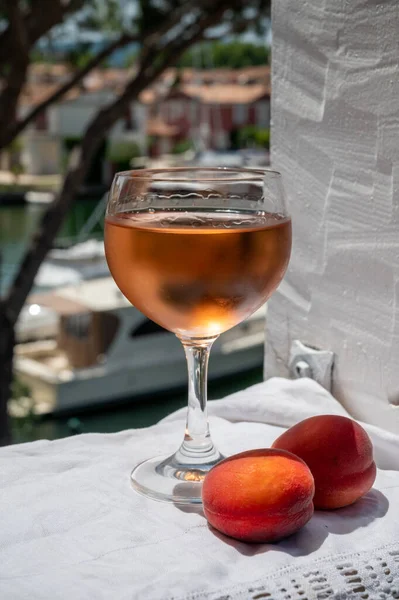 Drinking of cold rose wine from Provence with red apricots and view on yacht harbour of Port Grimaud, summer vacation on French Riviera, France