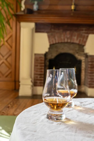 Two drams of scotch whiskey with view on fireplace in old house on background, Edinburgh whisky tasting tour, Scotland
