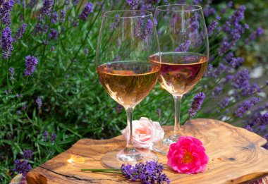 Provence 'den Fransız gülü şarabı, arka planda mor lavanta çiçekli iki kadeh şarap güneşli bir günde açık havada zeytin ağacı tahtasında servis ediliyor.