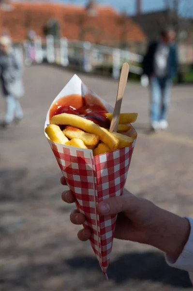 Dutch and Belgian fast and street food, child\'s hand with paper bag of fried potatoes chips with tomato ketchup