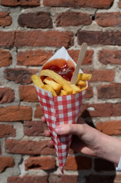 Dutch and Belgian fast and street food, child\'s hand with paper bag of fried potatoes chips with tomato ketchup