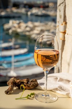 Soğuk gül şarabı, cam içinde sunulan güneş ışığı eşliğinde açık terasta, Cassis, Provence, Fransa 'da eski balıkçıların limanında renkli teknelerle sunuluyor.