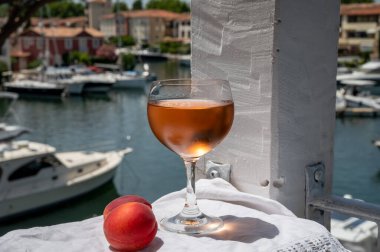 Drinking of cold rose wine from Provence with red apricots and view on yacht harbour of Port Grimaud, summer vacation on French Riviera, France