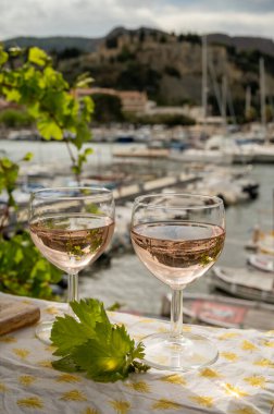 Açık terasta sunulan Rose Provencal şarabı Cassis, Provence, Fransa 'da renkli tekneleri olan eski balıkçıların limanına bakıyor.