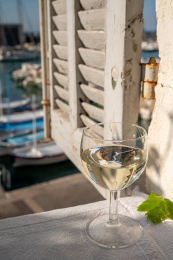 Cassis şarap üretim bölgesinden bir bardak beyaz şarap açık terasta eski balıkçıların limanı manzaralı Cassis, Provence, Fransa 'da renkli teknelerle servis ediliyor.