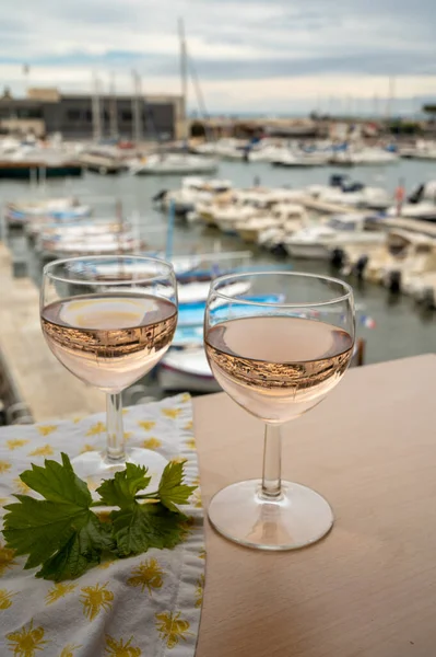 Açık terasta sunulan Rose Provencal şarabı Cassis, Provence, Fransa 'da renkli tekneleri olan eski balıkçıların limanına bakıyor.