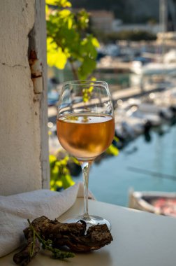 Soğuk gül şarabı, cam içinde sunulan güneş ışığı eşliğinde açık terasta, Cassis, Provence, Fransa 'da eski balıkçıların limanında renkli teknelerle sunuluyor.