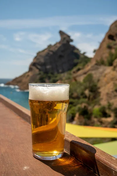 Glass of fresh cold lager beer served outdoor in snack bar with view on Calanque de Figuerolles in La Ciotat, Provence, France in sunny day