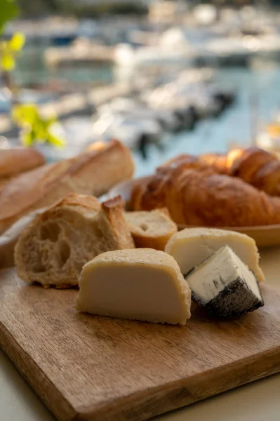 Provence 'de güneşli bir sabah, taze kruvasan, baquett ekmeği, crottin keçi peyniri ve Cassis, Provence, Fransa limanındaki balıkçı tekneleri manzaralı bir kahvaltı.