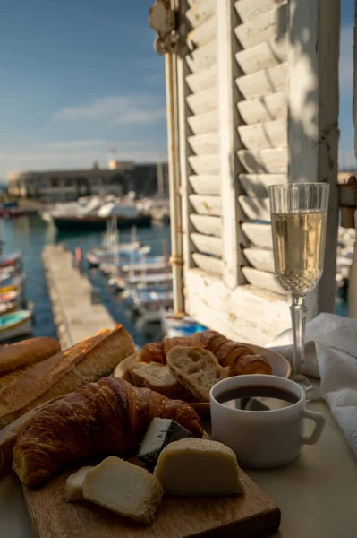 Fransız kahvaltısında taze kruvasan, baquett ekmeği, crottin keçi peyniri, sade kahve ve Cassis, Provence, Fransa 'daki balıkçı tekneleri manzaralı. Provence 'de Tatil.