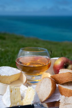Etretat 'ın tebeşir kayalıklarında yeşil çimen tarlalarında öğle yemeği, Fransız peynirli camembert peyniri, taze fırında baget ve elma şarabı, arka planda mavi Atlantik okyanusu, Normandiya, Fransa