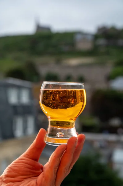 Hand holding one glass of apple cider drink and houses of Etretat village on background, Normandy, France