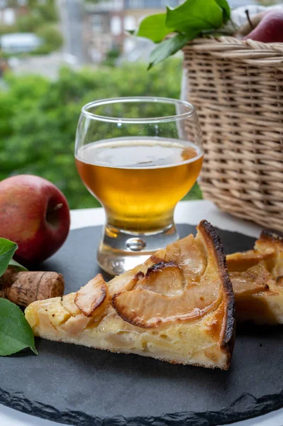 Apple products of Normandy region, homemade baked apple cake, glass of cider drink and houses of Etretat village on background, Normandy, France