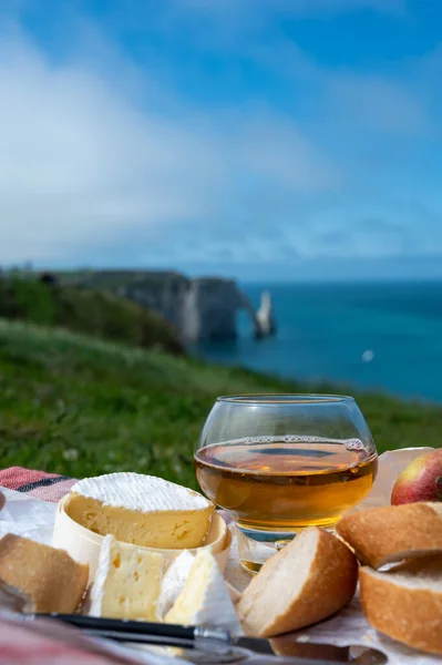 Lunch on green grass fields on chalk cliffs of Etretat, french cheese camembert, fresh baked baguette and apple cider drink with blue Atlantic ocean on background, Normandy, France