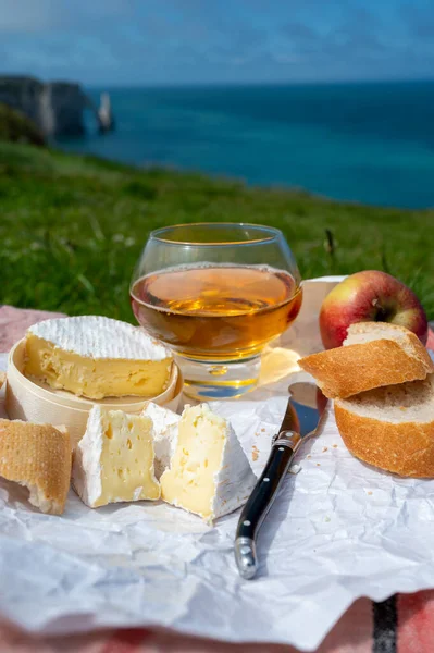 Lunch on green grass fields on chalk cliffs of Etretat, french cheese camembert, fresh baked baguette and apple cider drink with blue Atlantic ocean on background, Normandy, France