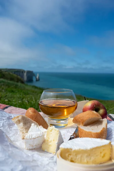 Lunch on green grass fields on chalk cliffs of Etretat, french cheese camembert, fresh baked baguette and apple cider drink with blue Atlantic ocean on background, Normandy, France