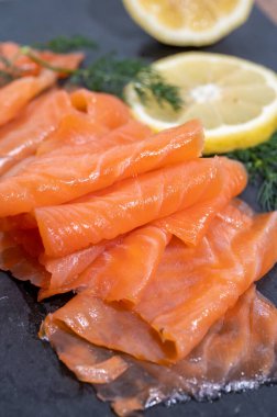Slices of tasty smoked Scottish salmon fish served on black plate with lemon and fresh dill close up